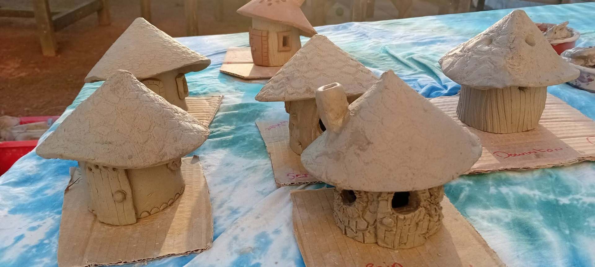 Row of handmade clay fairy houses drying after a community pottery workshop