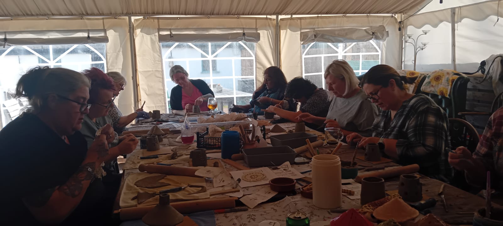 Long marquee table of participants hand-building clay pots and figures